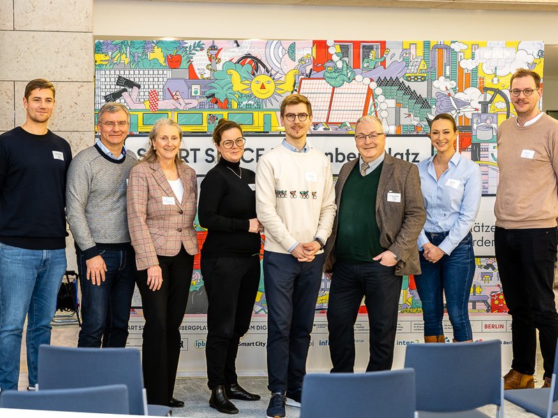 The photo shows eight experts from the panel, standing next to each other in front of the exhibition wall of the project SMART SPACE Hardenbergplatz.