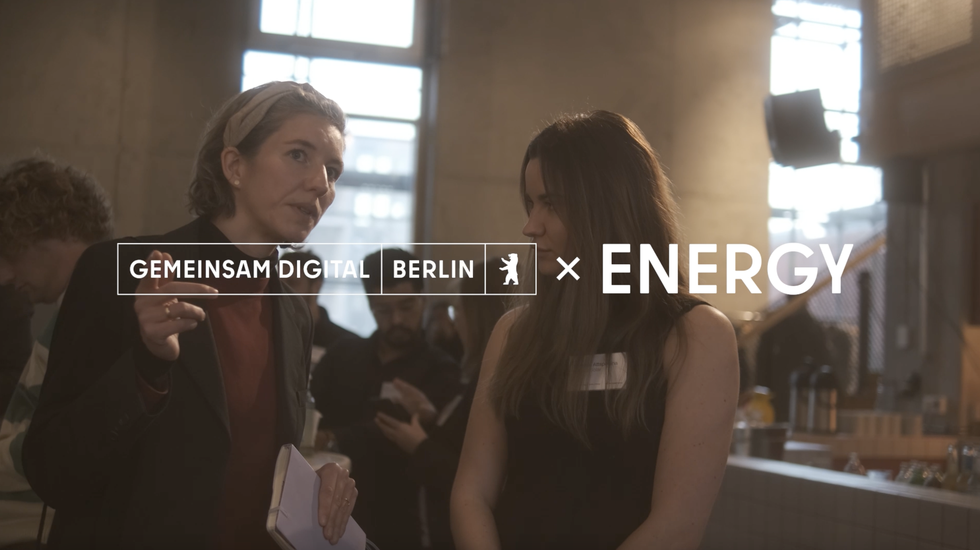 Zwei Personen, die sich unterhalten und im Vordergrund das Gemeinsam Digital: Berlin X Energy Video